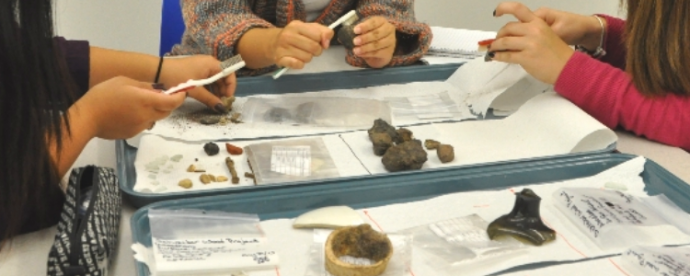 close up of three students' hands working on small archaeological artifacts in a lab classroom