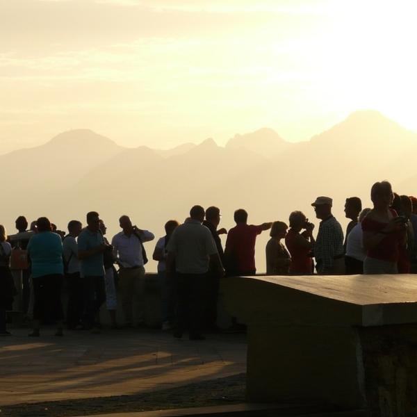 Group of people in silhouette outside against a background of sky and mountains.