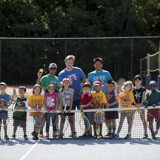 Group photo of children camp attendees with camp counsellors at the tennis court