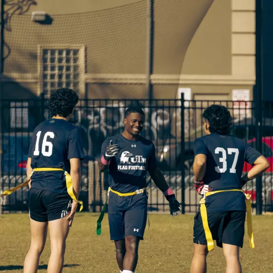 Group of men in an outdoor field giving each other high fives in the middle of a flag football game