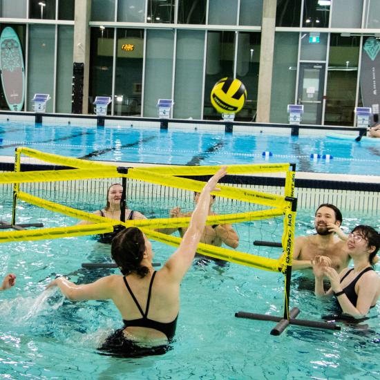 Group of people in an indoor swimming pool playing water volleyball