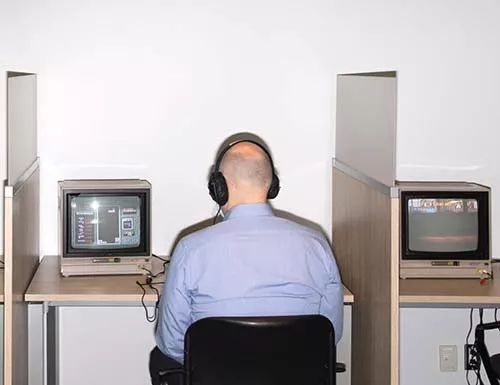 Man seated in a cubicle, playing video games at the Bolton Collection
