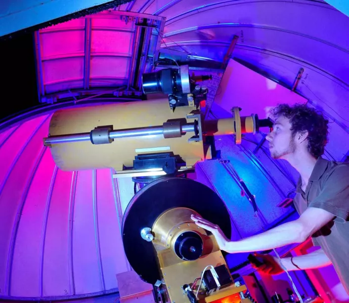Astronomy student using a telescope within an observatory at night