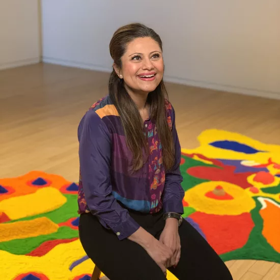 Noni Kaur seated on a stool with her art installation behind her at a gallary