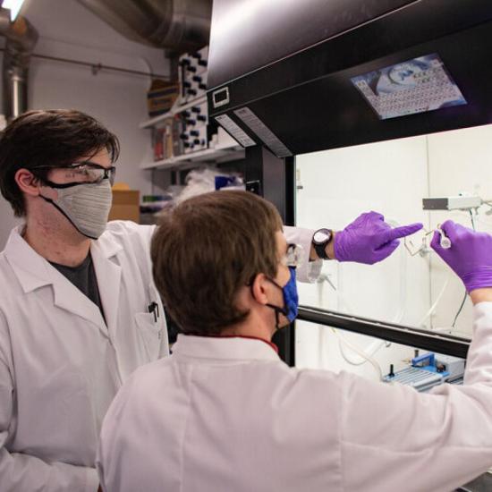 Two male students in a lab wearing lab coats conducting an experiment