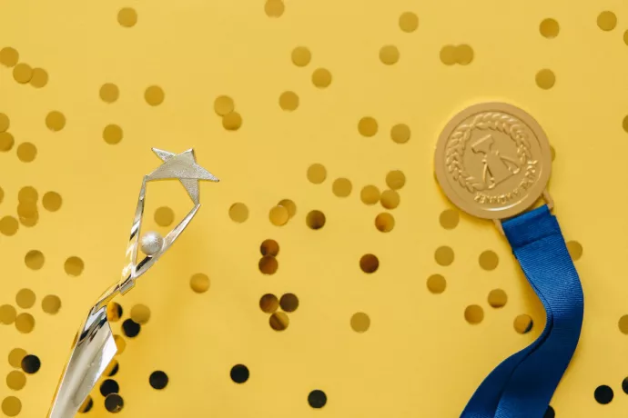A medal and a trophy against a yellow backdrop with confetti