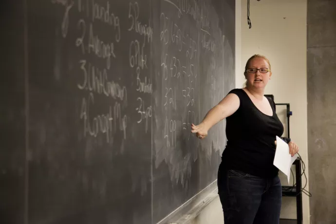 A teaching assistant pointing to information on a blackboard
