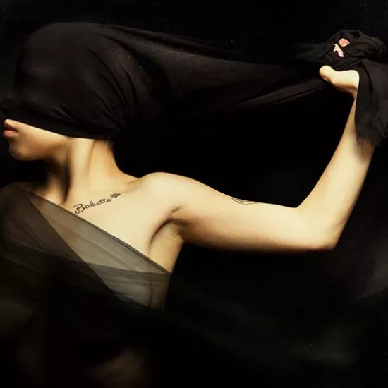 Artistic photo of woman holding a sheer black sash with a tattoo on her lower neck