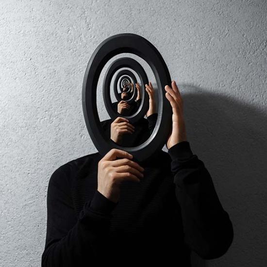 Person in black holding a mirror with endless circles displayed inside