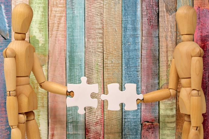 Two wooden figures putting puzzle pieces together