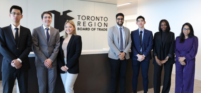 Group of six students standing in front of a board of trade sign