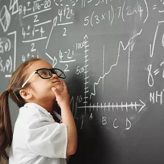 A young girl with pigtails standing in front of a blackboard, holding her chin as if she is pondering about the mathematical equations written on the board.