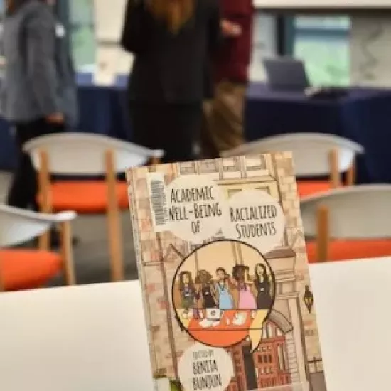 A book resting on a stand on top of a desk, with people conversing in the background.