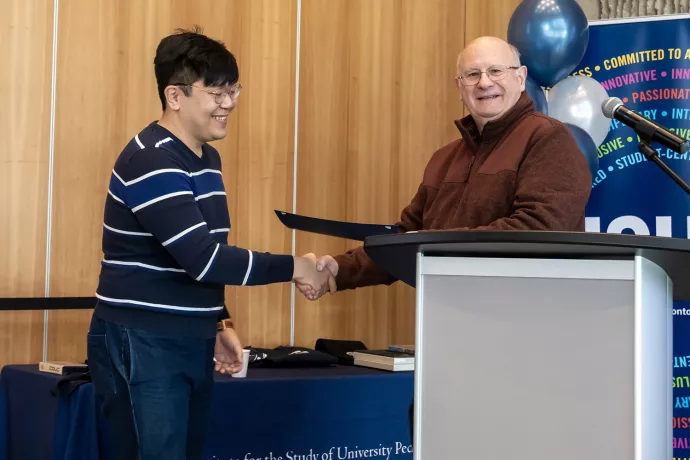 A man presenting an award to a student winner as they shake each other's hands at the podium.