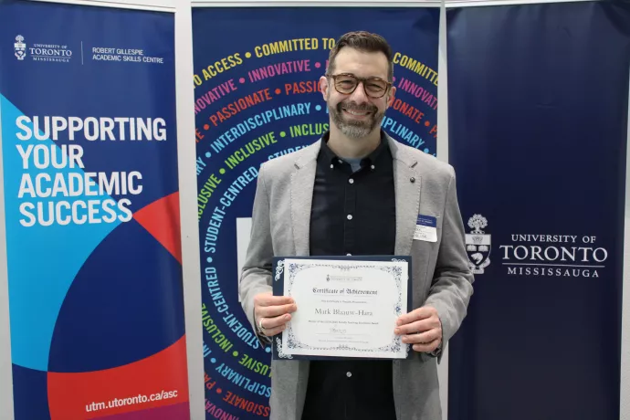Mark Blaauw-Hara holding his award certificate