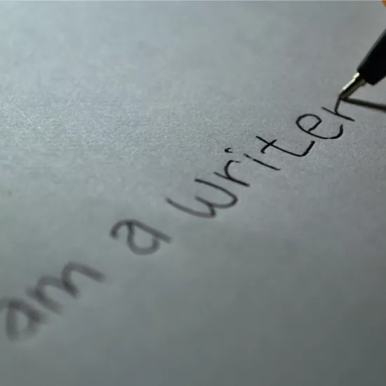 Pen writing on blank paper. Words read "I am a writer".