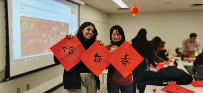 Two students hold up three red sheets of paper with Chinese calligraphy