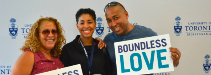 A family in front of a UTM backdrop, smiling. A parent is holding a sign saying "Boundless Love."