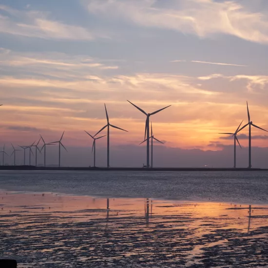 A sunset with wind turbines across a landscape with water in the foreground