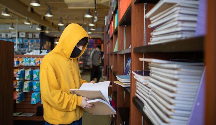 Student wearing a mask and reading a book while in the library