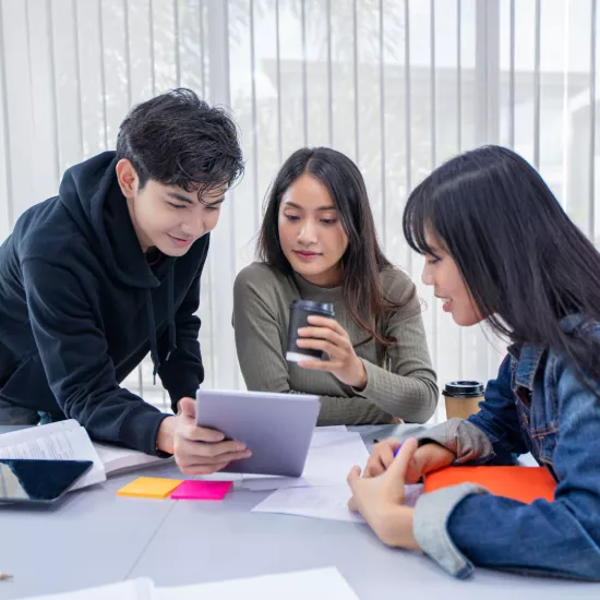 Three students sitting a table looking at a tablet.