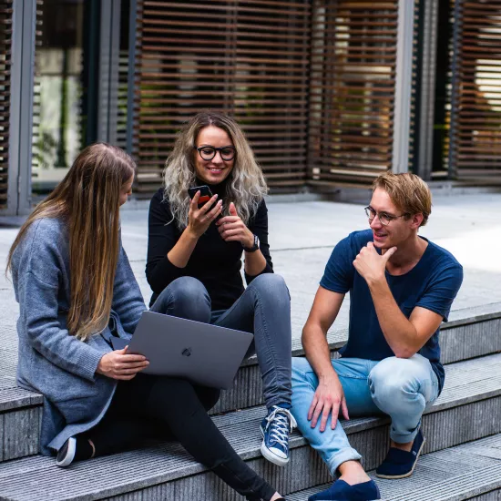 three students sitting on steps outside a building