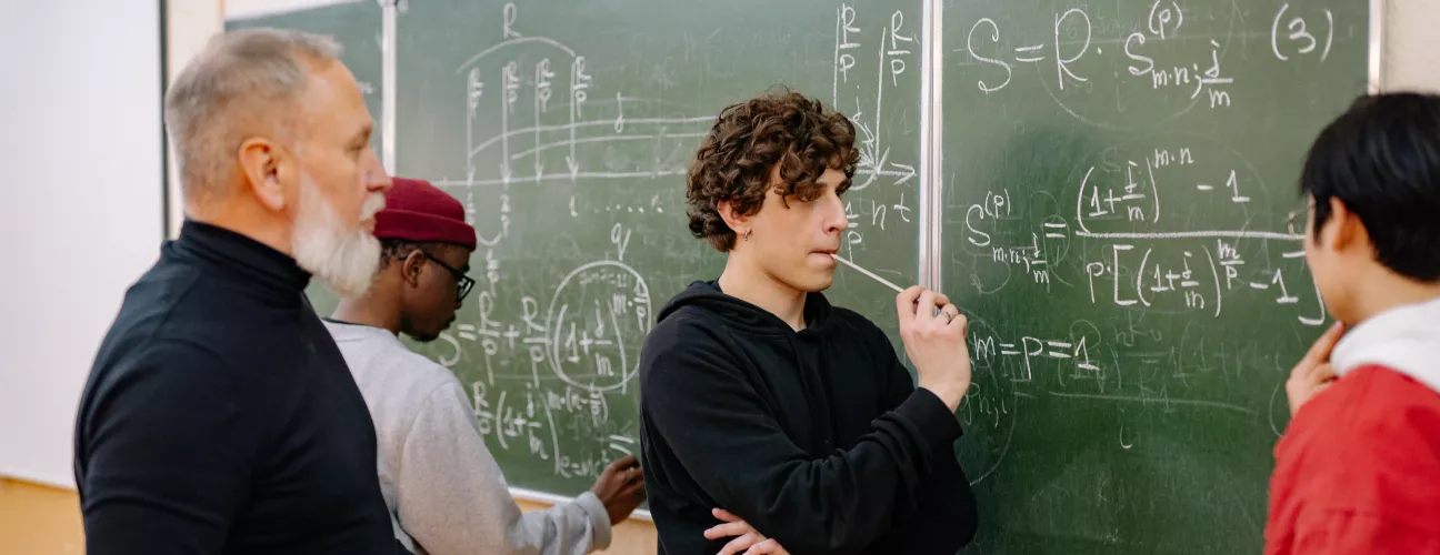 Three students and a professor standing in front of a chalkboard with math written all over it.