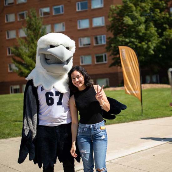 Student posing with the UTM Eagle in front of UTM residences 