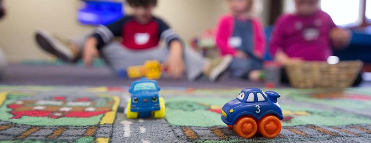 Toy cars and children sitting on a playmat in a daycare. Photo by BBC Creative on Unsplash