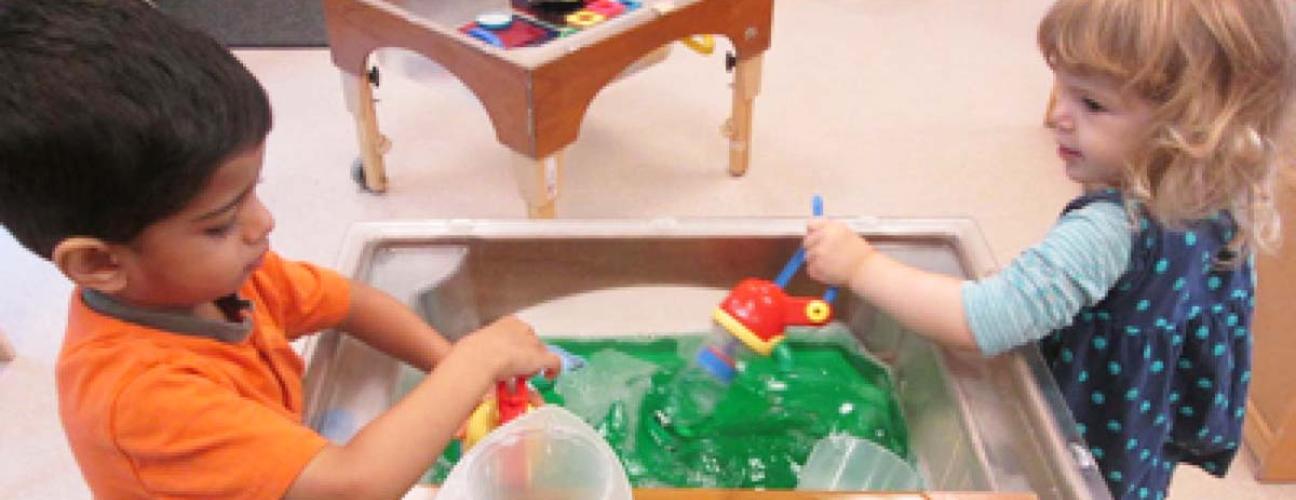 Two children playing at a water table in daycare classroom