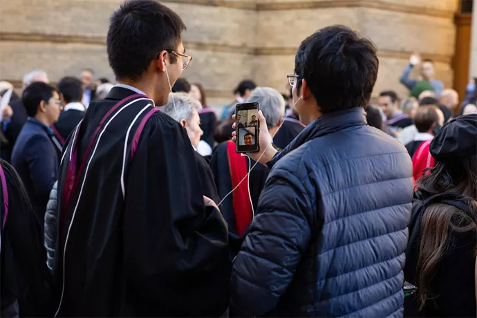 A graduate standing outside video calling on their phone.