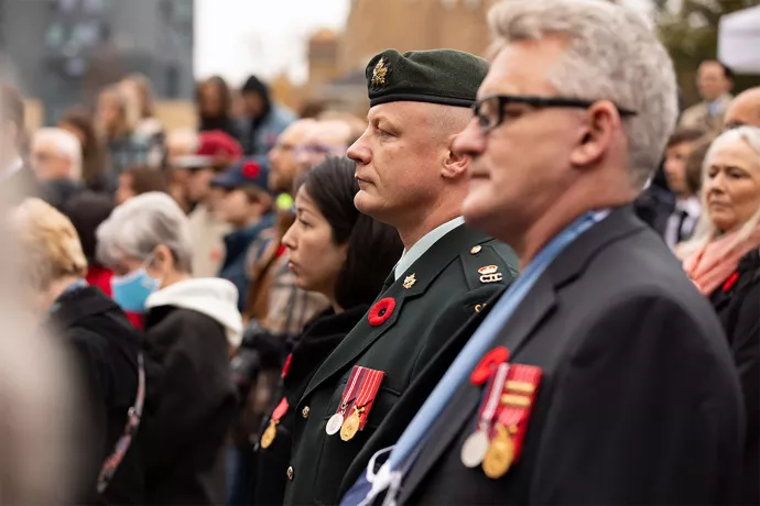 Rows of people stand facing the Remembrance Day ceremony, some wearing military uniforms