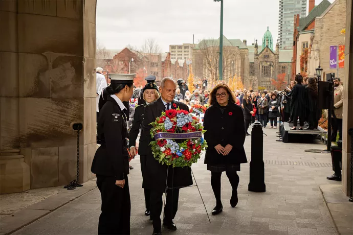 President Meric Gertler walks toward camera holding a Remembrance Day wreath with poppies on it