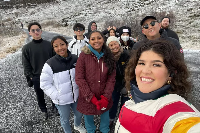 10 students posing for a selfie style photo with lightly snow covered hills in the background.