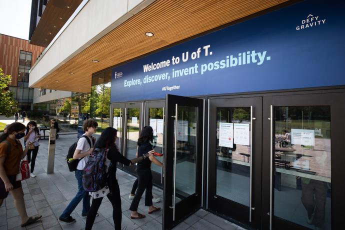 Students walking through glass doors with sign above doors that reads Welcome to U of T. Explore, discover, invent possibility