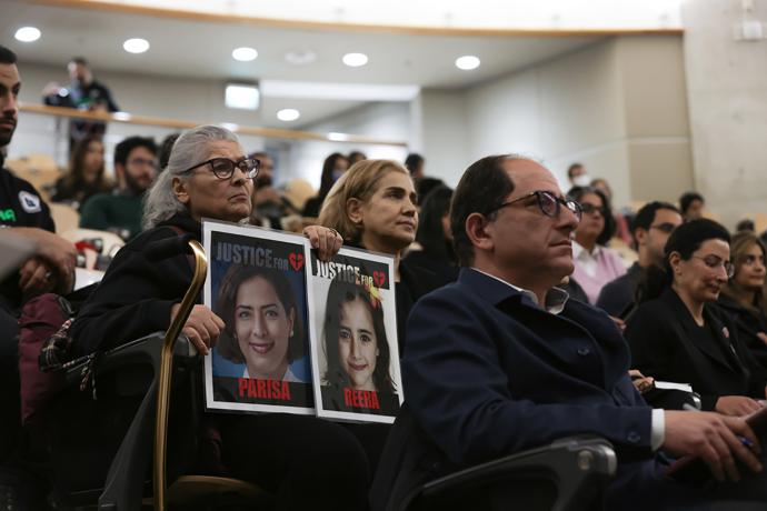 People sit in an auditorium, one woman holding up two photos of women which both read Justice above the photos.