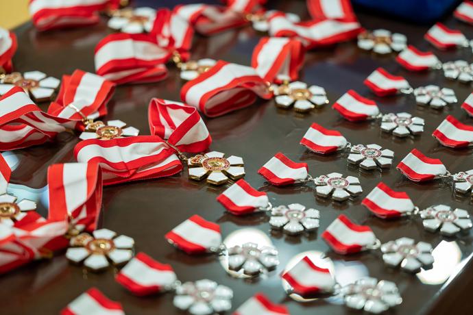 Row of medals on black table. Medals include a ribbon on top that has a thinner red stripe on either side of a wide white strip in the middle. The medal has six points.