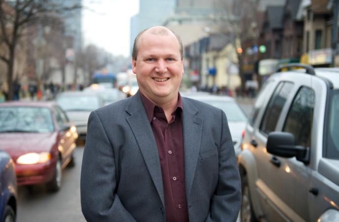 Greg Evans stands on a city street, surrounded by cars