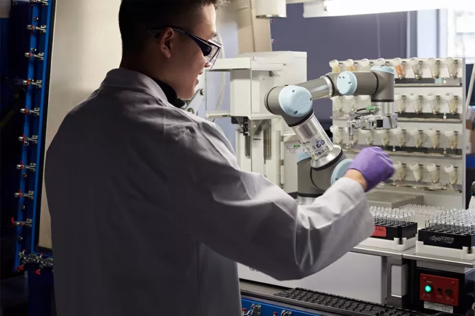 Researcher in white lab coat and gloves works on task in a lab