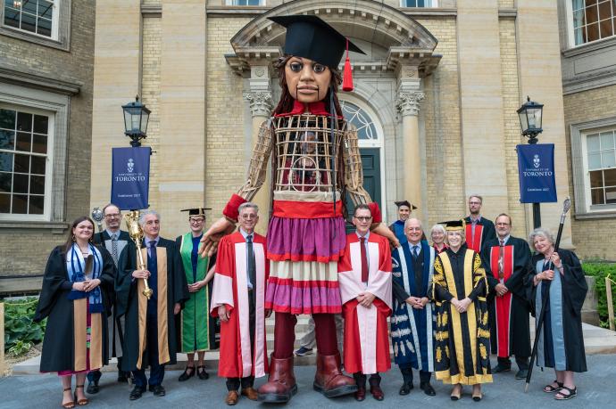 Group photo of academic procession members with Little Amal and honorary degree recipients Basil Jones and Adrian Kohler