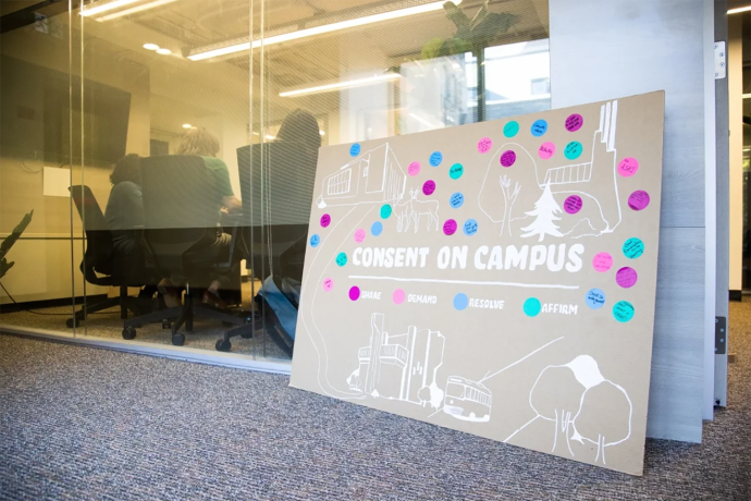 Large board leaning against glass partition that reads Consent on campus