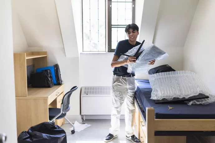A student unpacks his bags in a residence room.