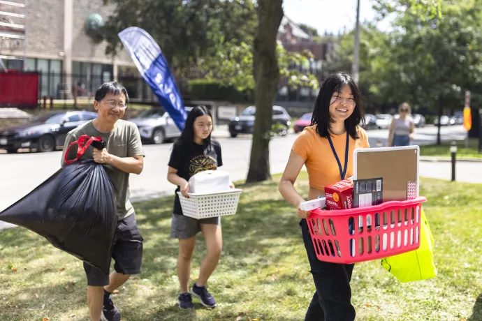 Students carry their belongings across a residence lawn.