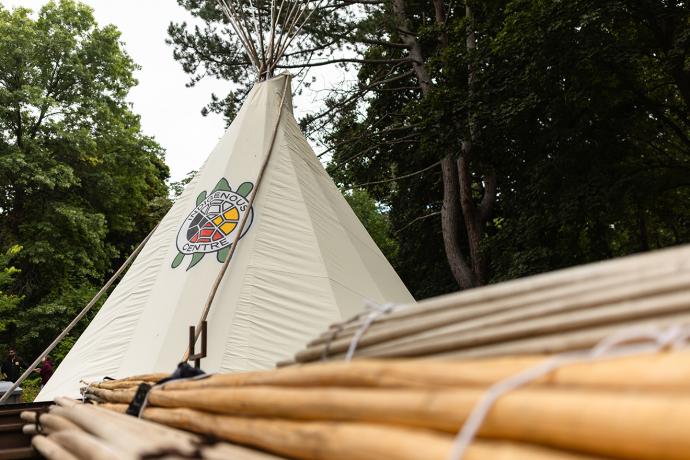 A Tipi is seen completed and surrounded by trees.