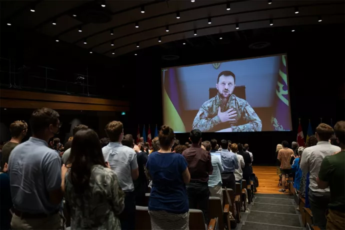 Volodomyr Zelenskyy is shown speaking on a large screen as students in Innis College watch.