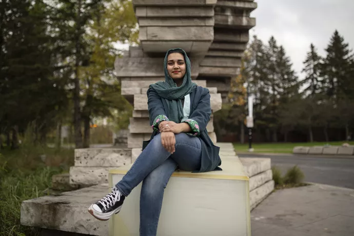 Amna Adnan sitting on the end of the stone entrance to UTM, smiling at the camera.