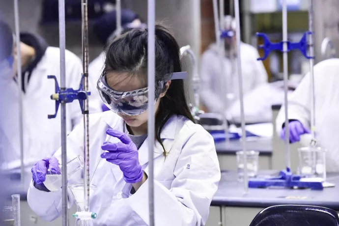 Woman in white lab coat, safety goggles and purple gloves does scientific experiment