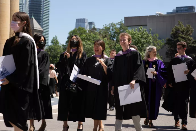 Grads walk out of Convocation Hall in a procession, wearing their regalia and holding degrees