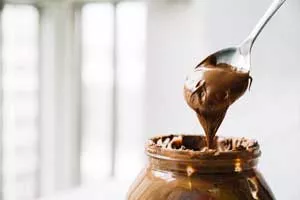 Photo of a jar and a spoon heaped with chocolate spread.
