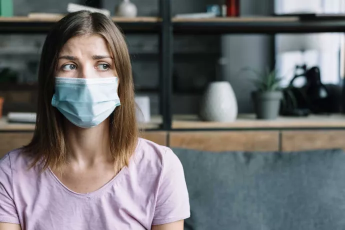 A sick young woman wearing a blue surgical mask.